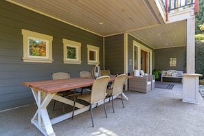 An outdoor patio with a wooden table and wicker chairs, a covered seating area, and a sign reading "LIFE WELCOME".