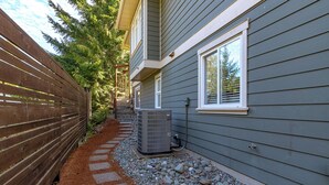 A residential building with a grey exterior, a wooden fence, a stone pathway, and an air conditioning unit. -  2 Bedroom Suite @ Shawnigan Suite Bed and Breakfast (Shawnigan Lake)