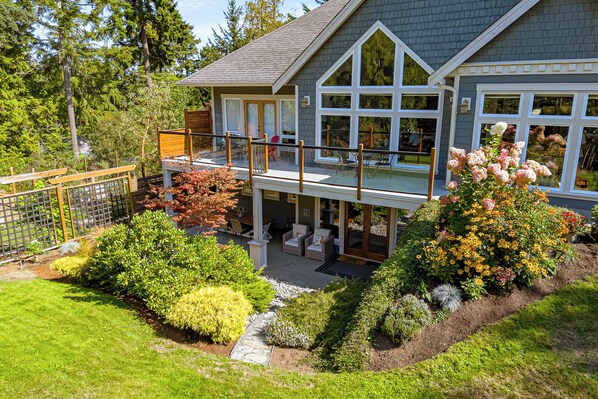 A two-story house with a balcony, a covered patio, and a well-maintained garden. - 2 Bedroom Suite @ Shawnigan Suite Bed and Breakfast (Shawnigan Lake)