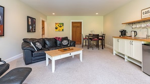A compact living space with a black leather sofa, a wooden coffee table, a dining table with chairs, and a kitchen area with white cabinets and a countertop.