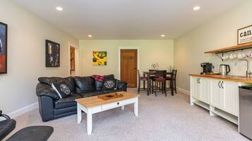 A compact living space with a black leather sofa, a wooden coffee table, a dining table with chairs, and a kitchen area with white cabinets and a countertop.