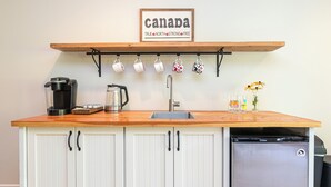 A kitchen with a wooden countertop, white cabinets, a sink, a coffee maker, a kettle, a toaster, a refrigerator, and a sign above the countertop that reads "canada true north strong free."