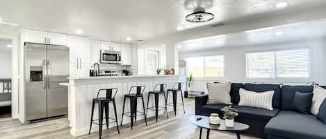 A modern kitchen with a central island, bar stools, a dark-colored sofa, and a patterned rug.
