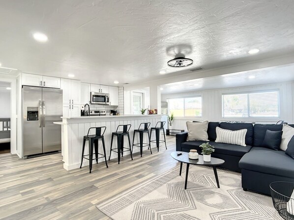 A modern kitchen with a central island, bar stools, a dark-colored sofa, and a patterned rug.
