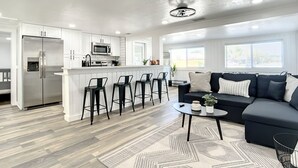 Una cocina moderna con una isla central, taburetes de bar, un sofá oscuro y una alfombra estampada.