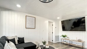 Una sala de estar moderna con un sofá seccional negro, una mesa de centro, un televisor montado en la pared y una alfombra estampada.