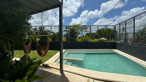 Piscina con cerramiento metálico, rodeada de follaje y un cielo despejado.