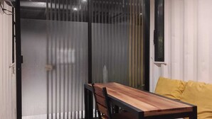 Una habitación moderna con una mesa de comedor de madera, un sofá con cojines amarillos y un ventanal con persianas verticales.
