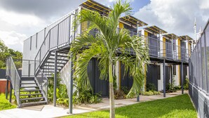 Un edificio moderno con fachada metálica, una escalera y un césped cuidado con una palmera.