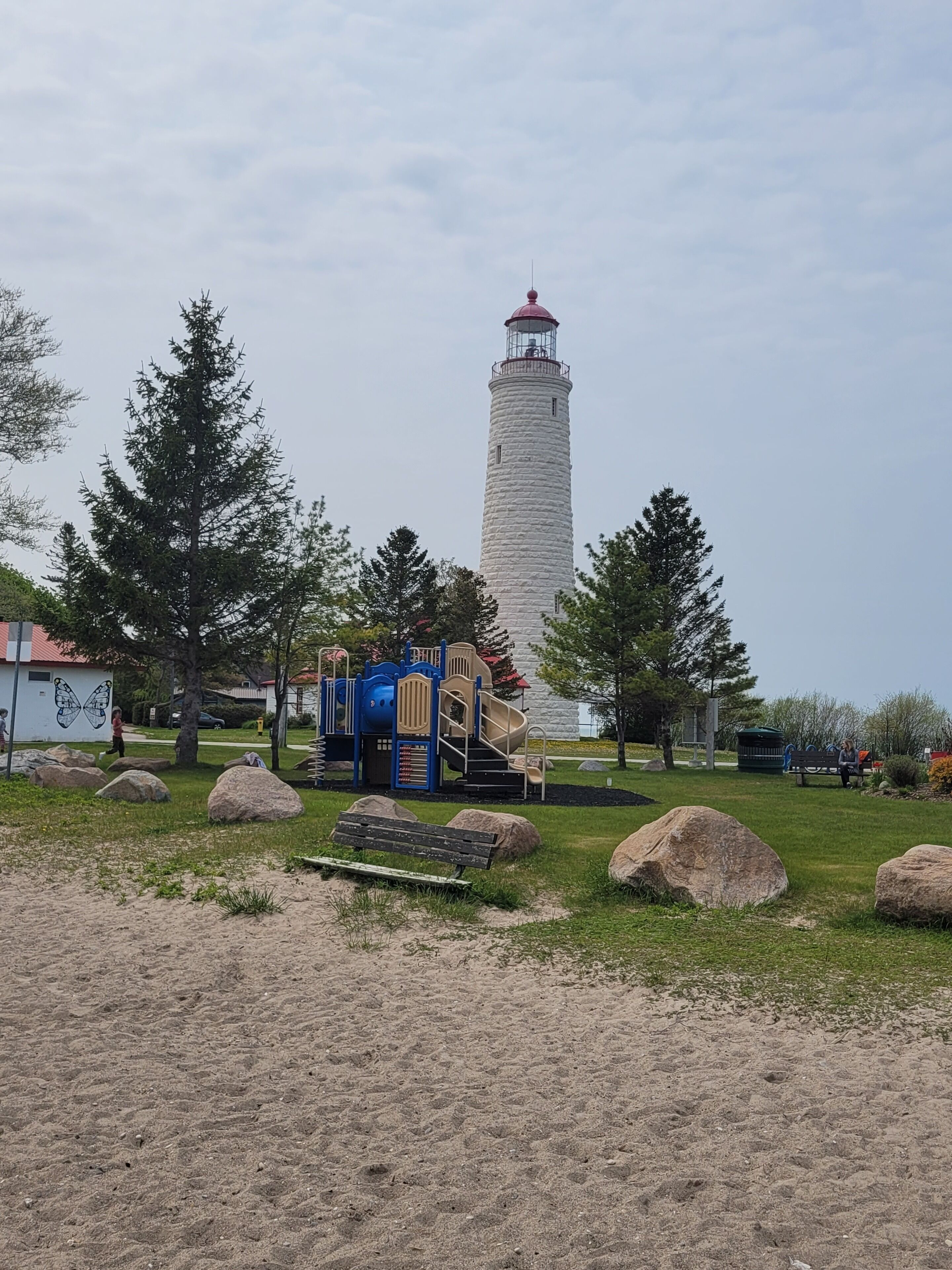 A lighthouse in a park with playground equipment and large rocks.