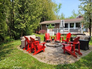 Eine Terrasse mit roten Adirondack-Stühlen, einem Rattansofa und einer Feuerstelle.