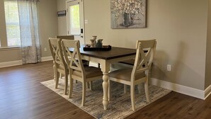 A dining room with a wooden table and four chairs, a rug, and a painting on the wall. - Plum Peachey - Bay St Louis (Bay St. Louis)