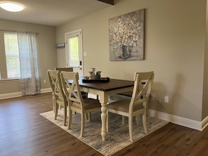 Un comedor con una mesa de madera y cuatro sillas, un tapete y un cuadro en la pared.