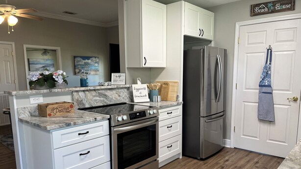 A kitchen with white cabinets, a stainless steel refrigerator, a built-in oven, and a marble countertop. - Plum Peachey - Bay St Louis (Bay St. Louis)
