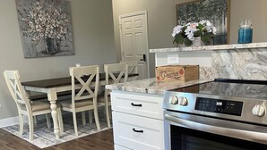 A kitchen with a built-in oven, a white countertop, and a dining area with a table and chairs. - Plum Peachey - Bay St Louis (Bay St. Louis)