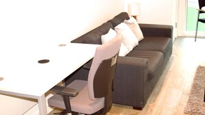 Een moderne woonkamer met een wit bureau, een grijze bank en een zwarte stoel.