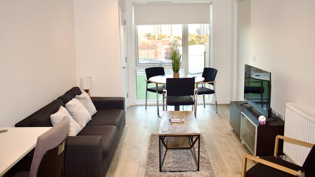 Een moderne woonkamer met een bank, salontafel, televisie en een eethoek met stoelen en een tafel.