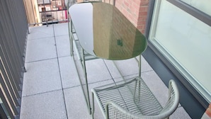 Een klein balkon met een metalen tafel en twee stoelen.