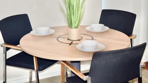 Een ronde houten tafel met vier zwarte stoelen, elk met een witte kop en schotel. Een gevlochten plantenpot staat in het midden van de tafel.
