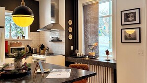 A modern kitchen with a central island, pendant lighting, and a view of a snowy landscape through a large window. - Victorian Apartment in the heart of Elora (Elora)