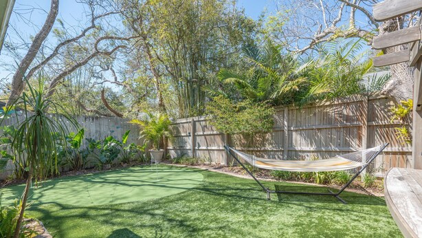 Un jardin avec un hamac, une clôture en bois et diverses plantes.