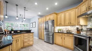 Une cuisine moderne avec des meubles en bois clair, des appareils électroménagers en acier inoxydable et des luminaires suspendus.