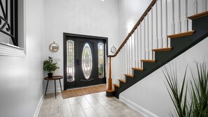 Un intérieur moderne avec un escalier noir et blanc, une porte décorative ornée de vitraux et une plante en pot.