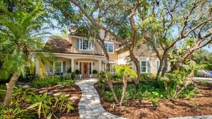 A two-story house with a stone pathway leading to the front door, surrounded by lush greenery and trees. - 2 LUX homes-1 PERFECT location -14BD/10BA-Heated Pool-WALK to beach-10 min to DT (St. Augustine)