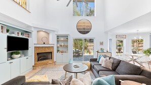A spacious living room with a fireplace, a ceiling fan, and a large window overlooking a garden. - 2 LUX homes-1 PERFECT location -14BD/10BA-Heated Pool-WALK to beach-10 min to DT (St. Augustine)