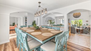 A spacious dining area with a wooden table and teal chairs, a hanging light fixture, and an arched doorway leading to another room. - 2 LUX homes-1 PERFECT location -14BD/10BA-Heated Pool-WALK to beach-10 min to DT (St. Augustine)