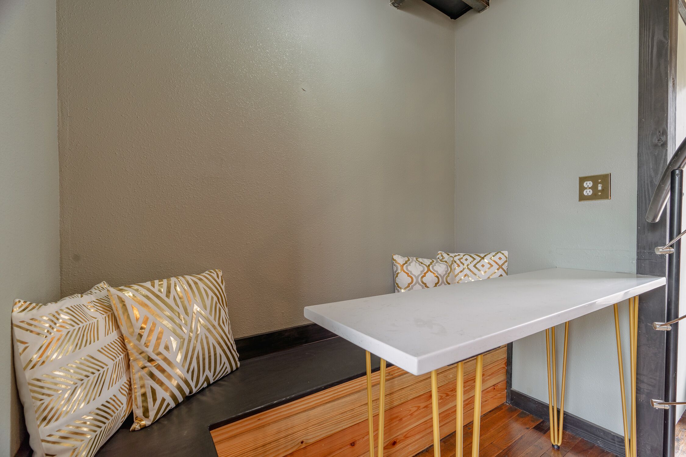 A corner room with a white table, a bench with patterned cushions, and a wooden bench with a black seat.