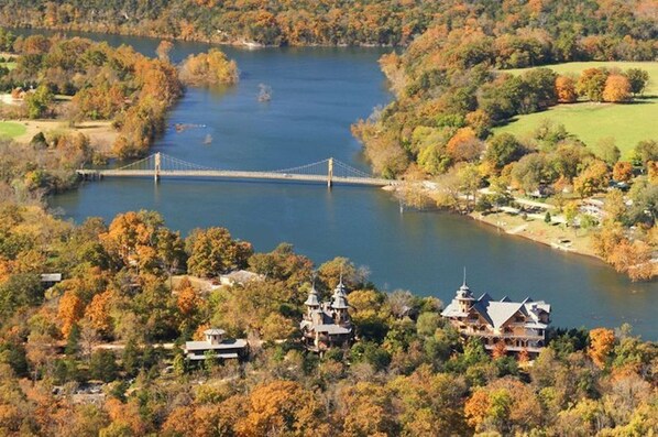 A bridge over a lake surrounded by autumn foliage and a large estate with multiple buildings. - 1870 Luxury Art Deco Train Depot at the Lake (Holiday Island)