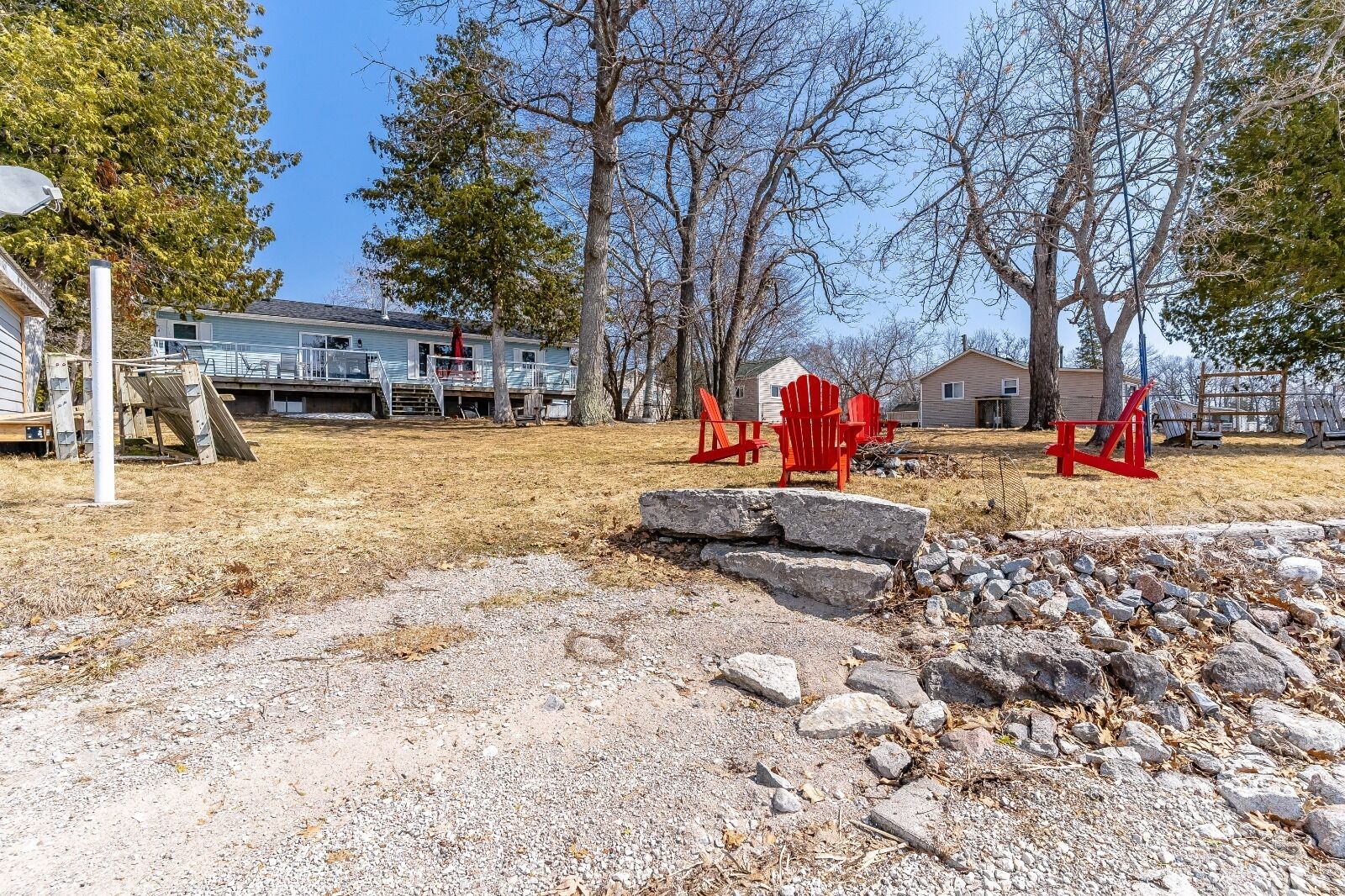A residential area with a gravel driveway, red Adirondack chairs, and a stone wall.