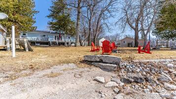 A residential area with a gravel driveway, red Adirondack chairs, and a stone wall.