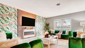A living room with a fireplace, green velvet sofas, a white coffee table, and a large window.