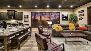 Un salon moderne avec un coin repas, un plafond en bois et une grande fenêtre offrant une vue sur le coucher de soleil.