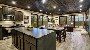 Une cuisine moderne avec des meubles de couleur bois foncé, un grand îlot central et un coin repas comprenant une table et des chaises.