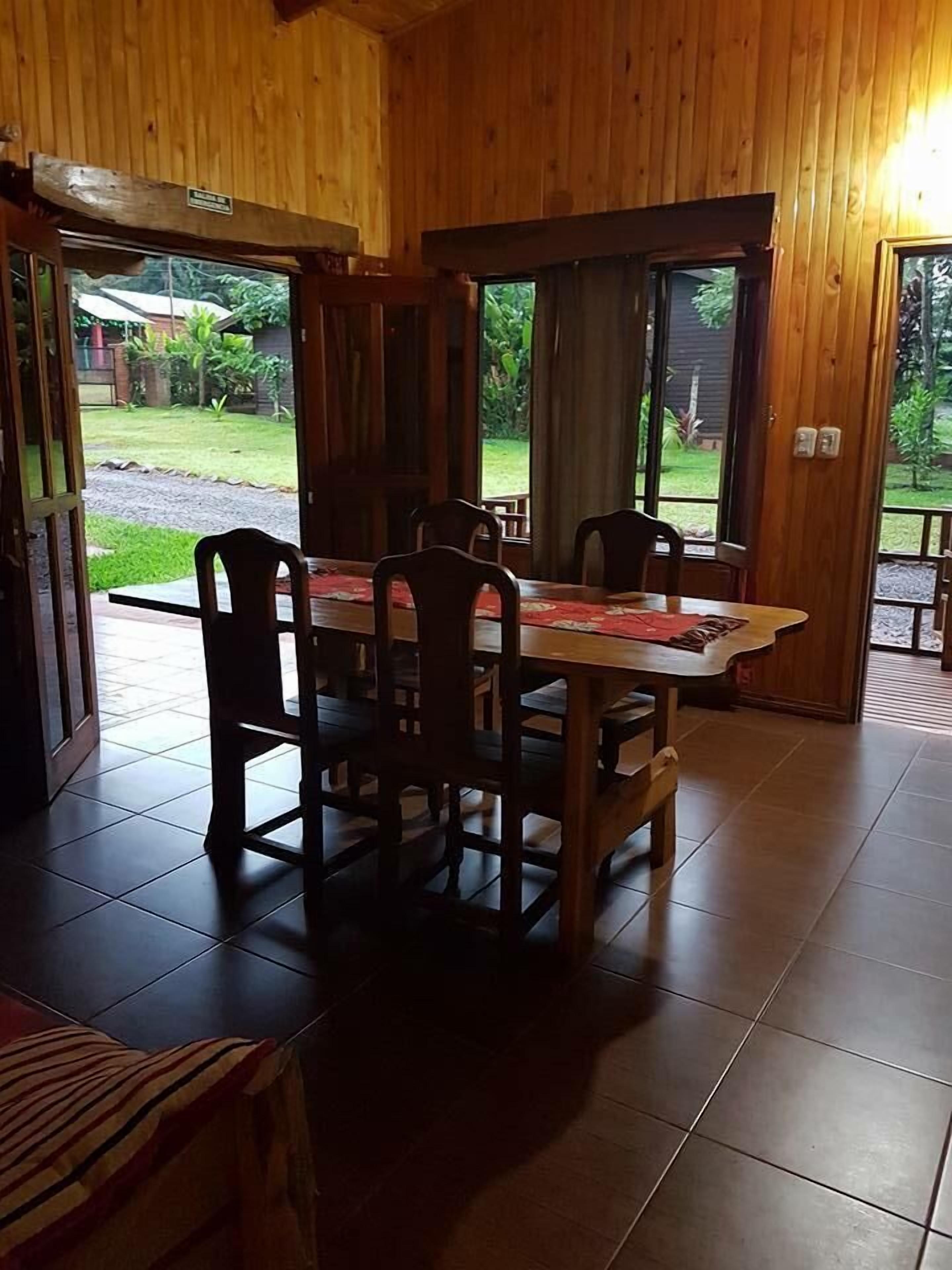 A wooden dining area with a table and chairs, large windows, and a view of the outdoors.