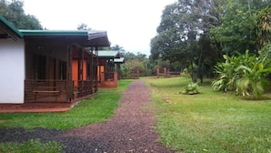 A pathway leading to a row of wooden cabins with green roofs, surrounded by lush greenery. - Raices Pampeanas (Puerto Iguazú)