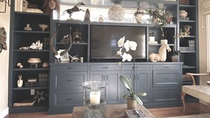 Una sala de estar con un mueble multimedia azul oscuro, estantes con libros y objetos decorativos, un florero de vidrio con una vela y una planta en maceta.