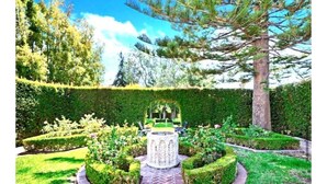 Un jardín cuidado con un estanque circular en el centro, rodeado de setos bien recortados y diversas plantas arbustivas.