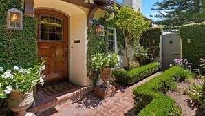 Una casa con puerta de madera, un camino de ladrillo y un jardín con diversas plantas y flores.