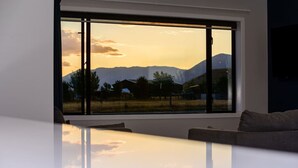 Et værelse med stort vindue og udsigt til bjerge og solnedgang.