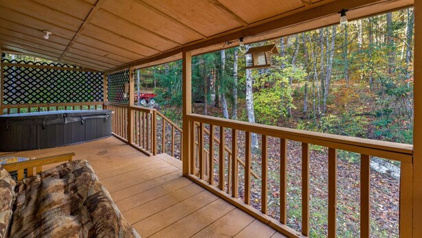 A covered deck with a wooden railing, a seating area, and a view of a forest. - Cozy and Private Smoky Mountain escape-perfect for a romantic getaway (Cosby)