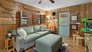 A cozy room with a green sofa, wooden walls, a ceiling fan, and a green arcade machine. - Cozy and Private Smoky Mountain escape-perfect for a romantic getaway (Cosby)