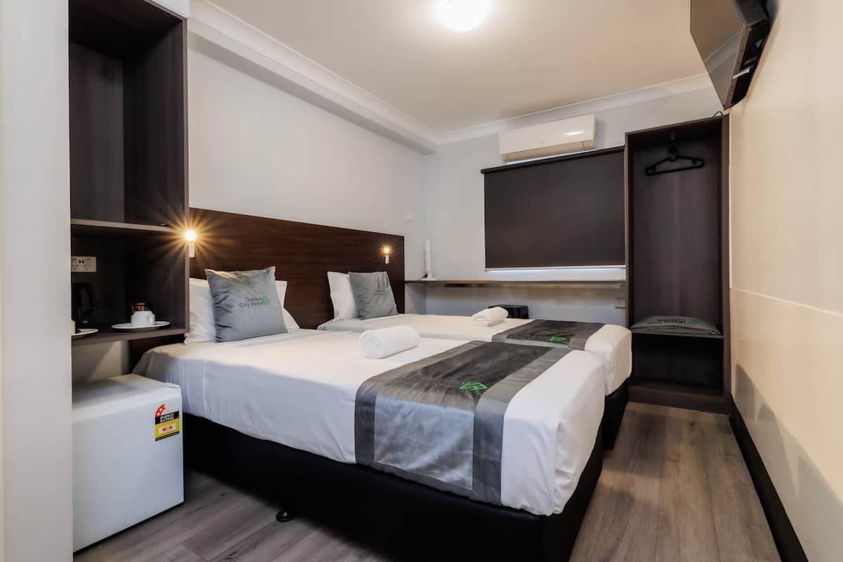 Habitación de hotel con dos camas, un minibar, un televisor y un perchero.