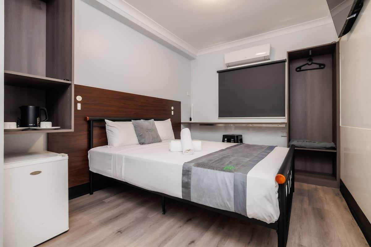 Habitación de hotel con una cama, un refrigerador pequeño blanco, una mesita de noche con cafetera, un perchero y un ventanal con vistas.