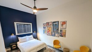 A bedroom with a bed, two chairs, a ceiling fan, and wall art. - Downtown 3 Bed Loft Apartment (Delaware)