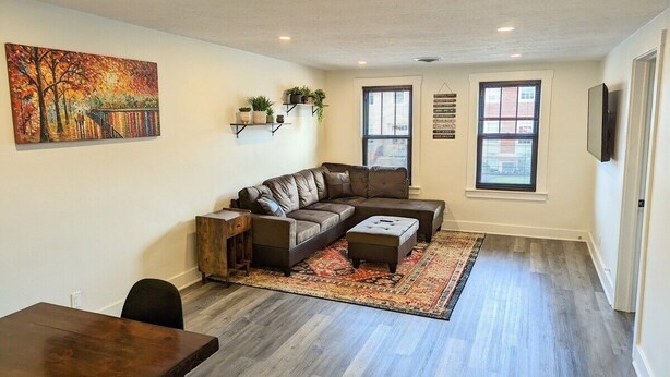 A living room with a sectional sofa, a coffee table, a rug, and a painting on the wall. - Downtown 3 Bed Loft Apartment (Delaware)
