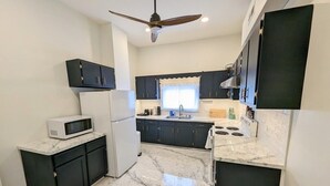 A compact kitchen with dark cabinets, a white refrigerator, a microwave, and a stove. - Downtown 3 Bed Loft Apartment (Delaware)